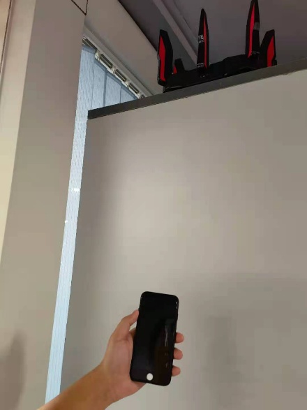 TP-Link router mounted high on a shelf with a hand holding a smartphone below to test signal.